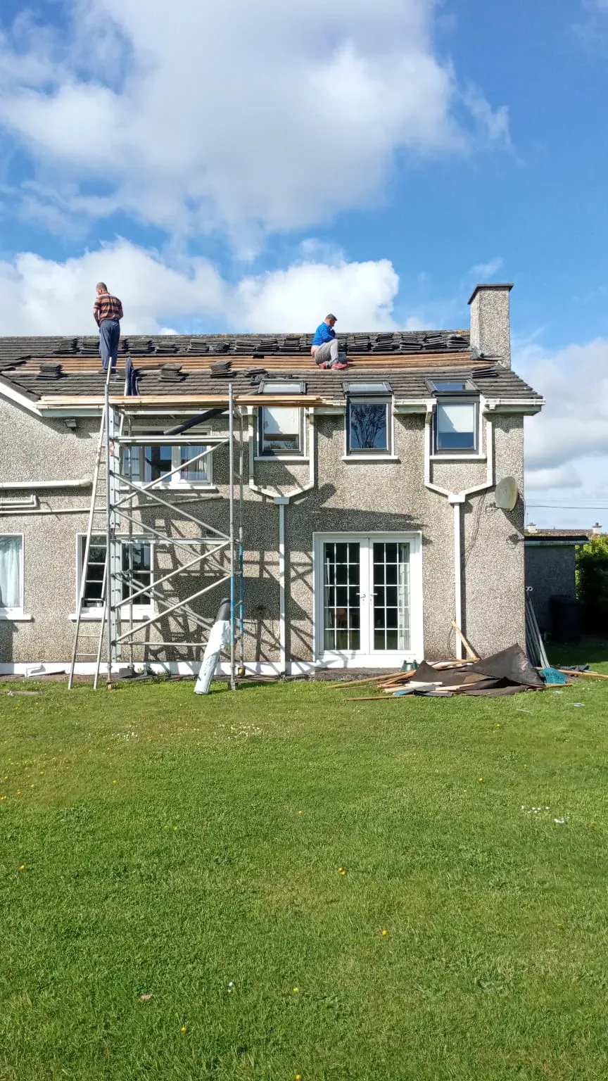 House with scaffolding up and roofers working at the roof edge