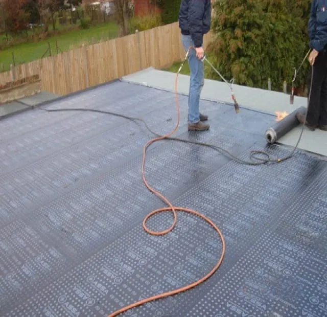 Torch-on felt being laid across a flat roof, with the burner hose on the deck